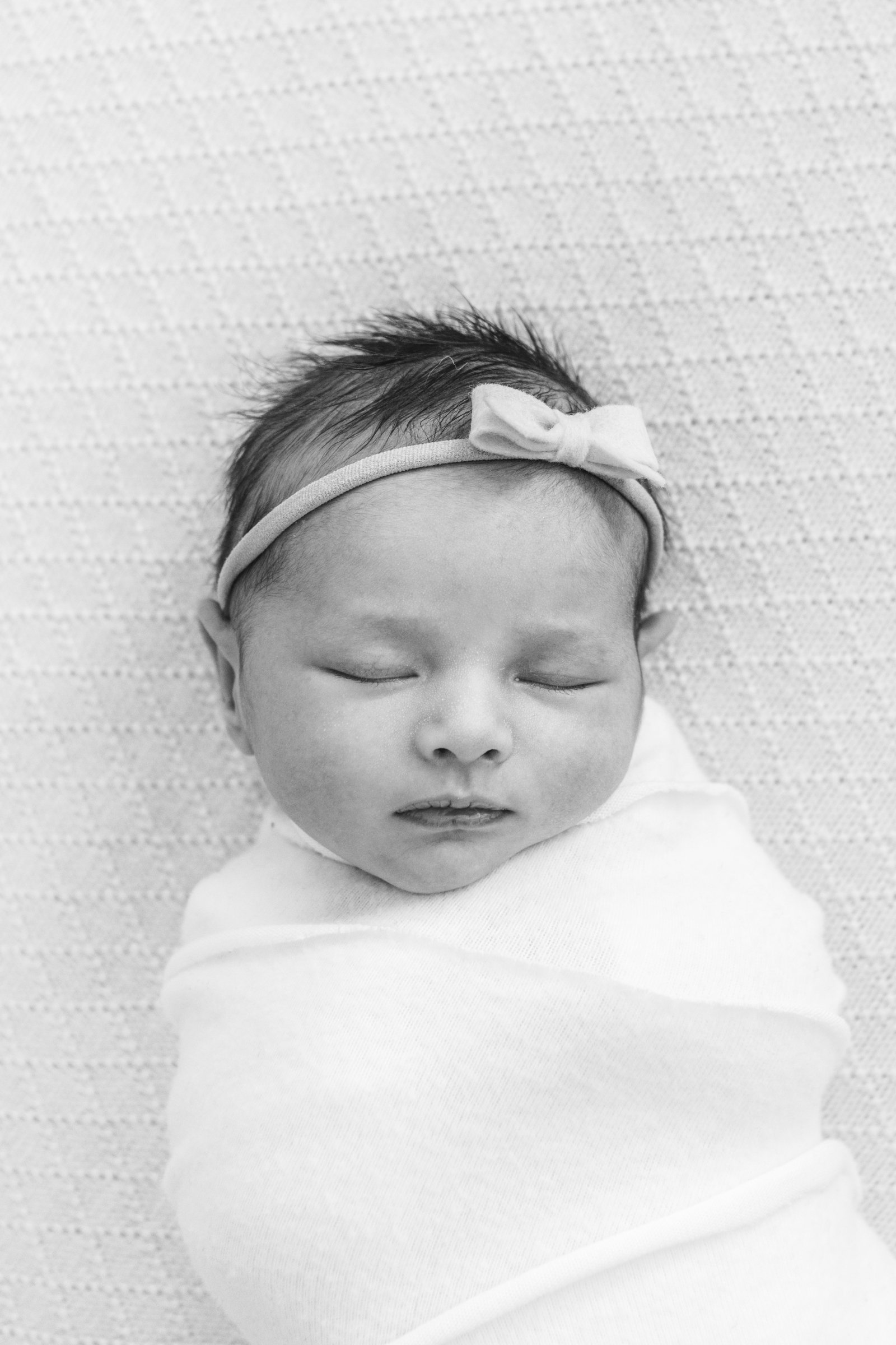  A baby girl with a nylon bow on her head and arms swaddled in a stretchy baby blanket sleeps peacefully as Nicole Hawkins Photography captures a tender moment in New Jersey. sleeping peaceful baby baby inspiration photos #nicolehawkinsphotography #n