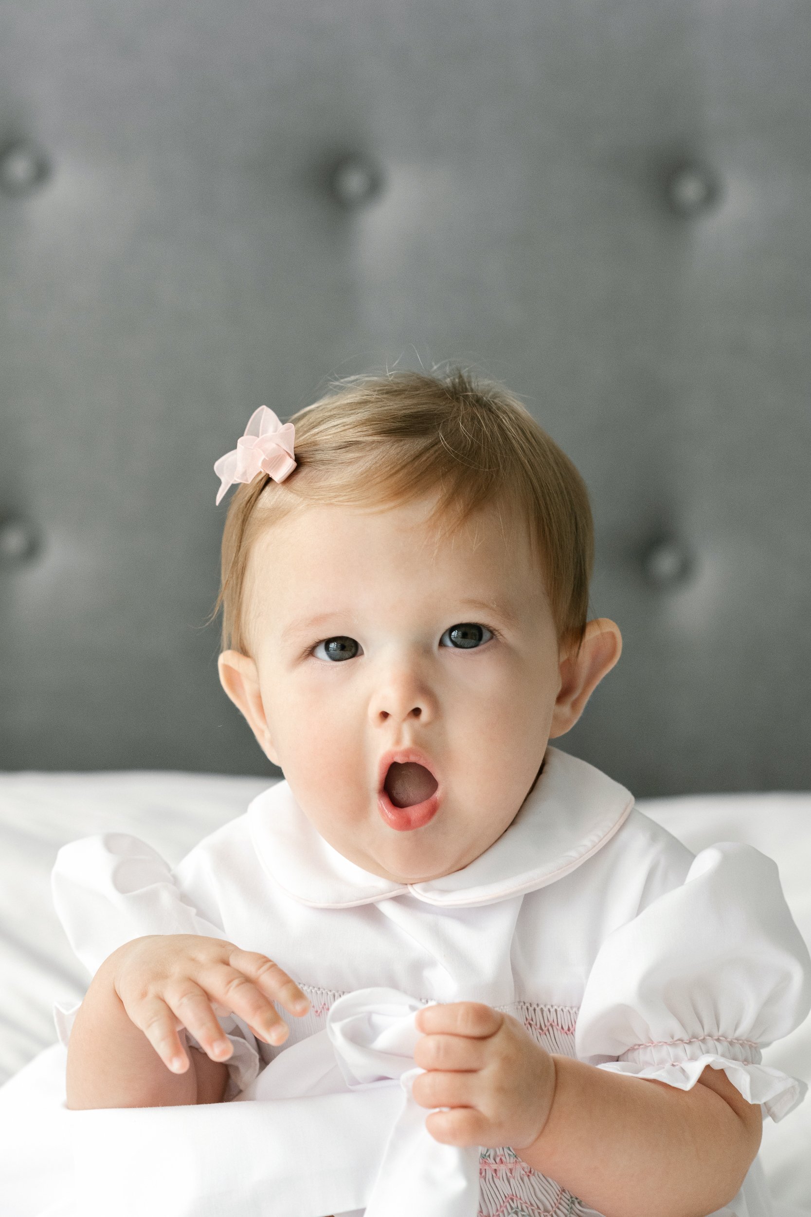  At a home session in New Jersey, a little girl makes a silly face by Nicole Hawkins Photography. white puffy sleeve dress milestone portraits #nicolehawkinsphotography #newjerseyphotographers #familyphotographer #6monthportraits #NJfamilyphotos 