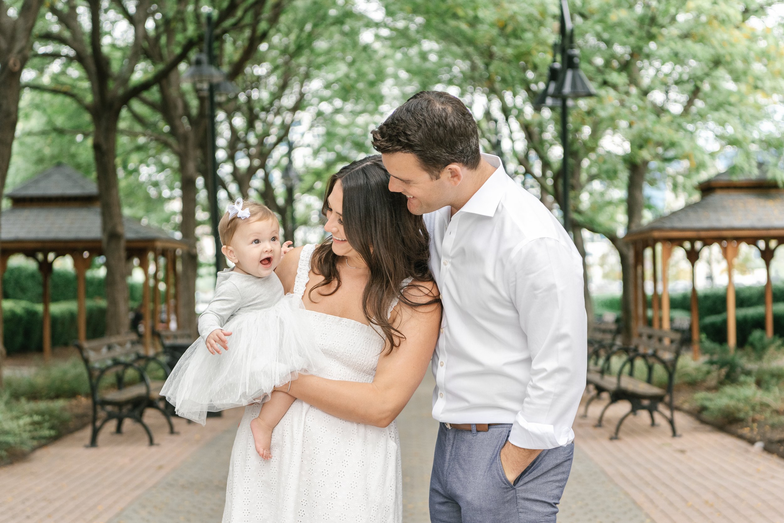  In New Jersey, Nicole Hawkins Photography captures a young family of three in a green park. New Jersey family photography Hoboken photos #nicolehawkinsphotography #newjerseyphotographers #familyphotographer #6monthportraits #NJfamilyphotos 