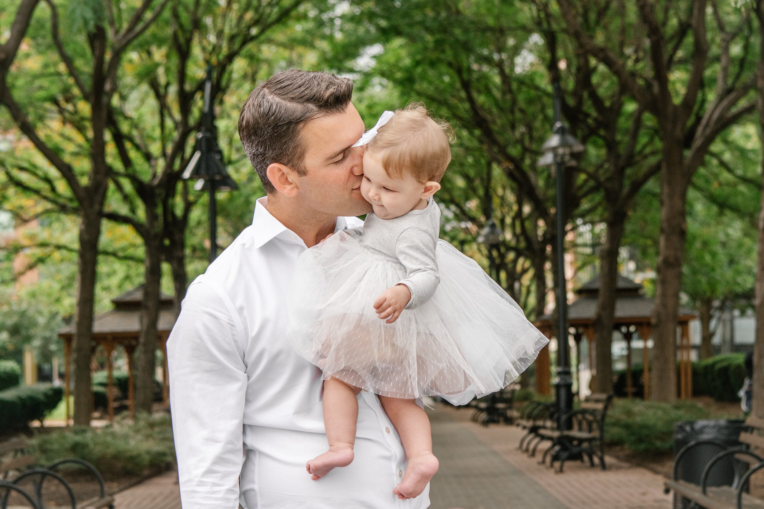 Father wearing a white button-up shirt kisses his baby girl on the cheek by Nicole Hawkins Photography. baby white tulle dress father kiss baby girl #nicolehawkinsphotography #newjerseyphotographers #familyphotographer #6monthportrait #NJfamilyphoto