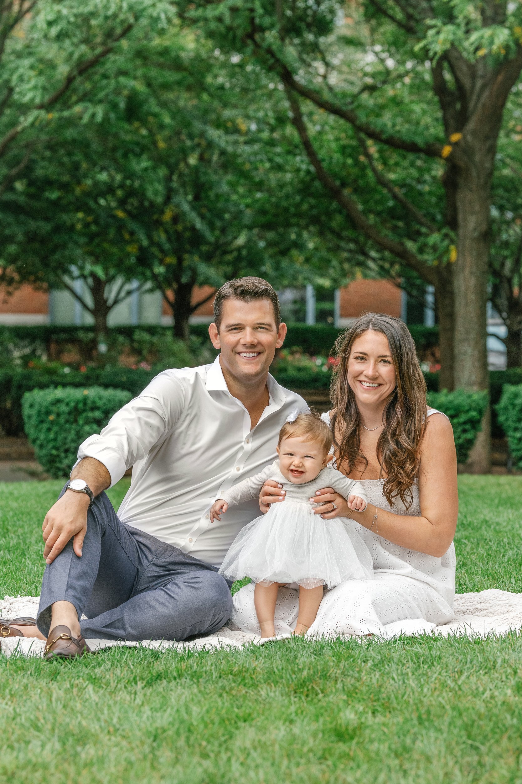  At a Hoboken park, a family with a baby sits on a picnic blanket captured by Nicole Hawkins Photography. family pictures with a baby girl #nicolehawkinsphotography #newjerseyphotographers #familyphotographer #6monthportraits #NJfamilyphotos 