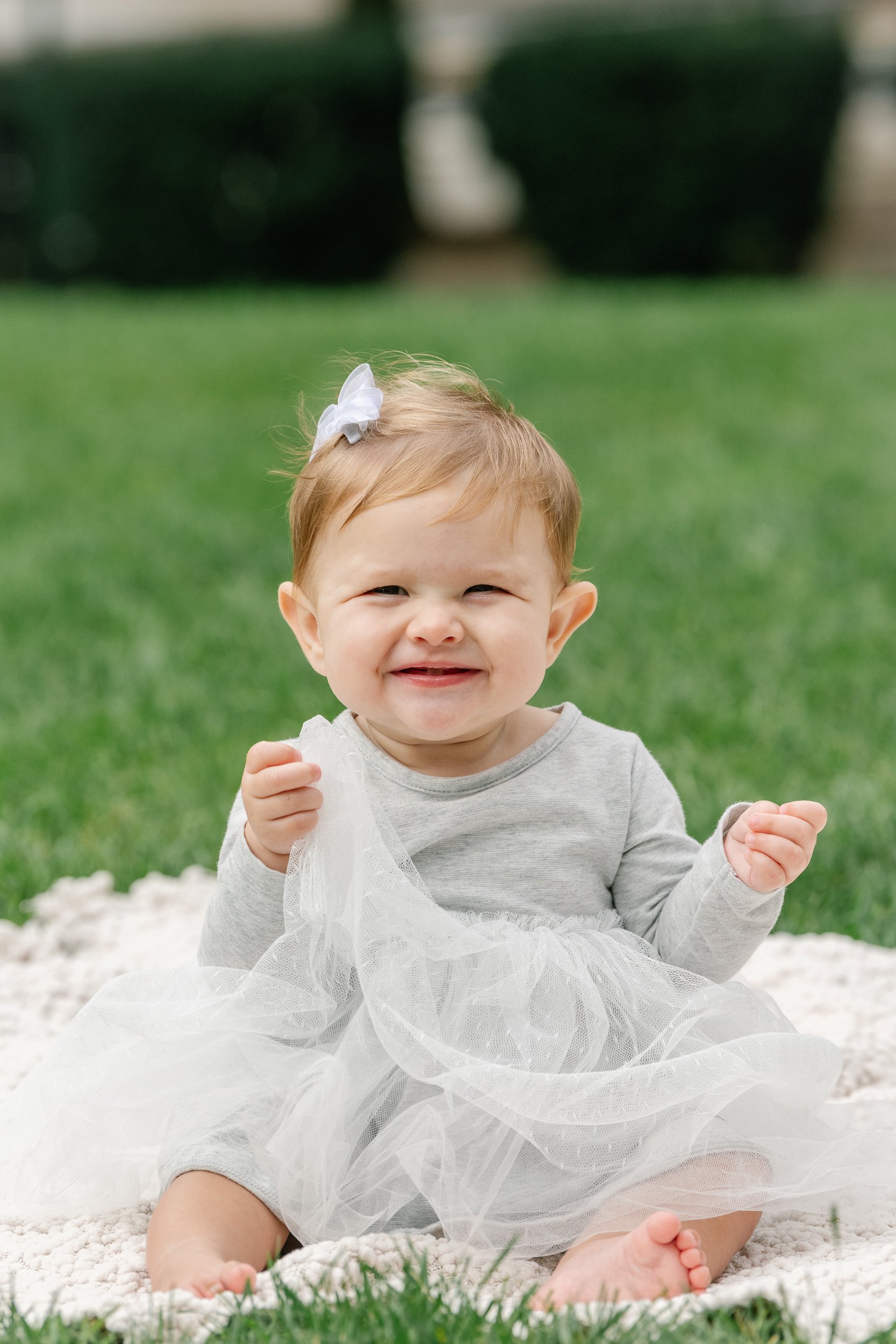  Nicole Hawkins Photography captures an infant girl sitting on a blanket wearing a gray sweater tulle dress. infant style NJ infant milestone pics #nicolehawkinsphotography #newjerseyphotographers #familyphotographer #6monthportraits #NJfamilyphotos 