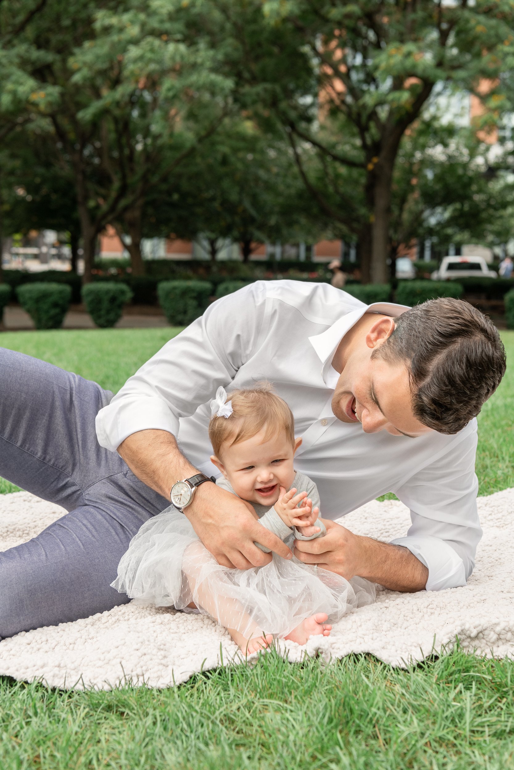  A new father helps his baby girl clap her hands in a New Jersey Park in the summer. gray tulle baby dress men's family picture outfits infant girl #nicolehawkinsphotography #newjerseyphotographers #familyphotographer #6monthportraits #NJfamilyphotos