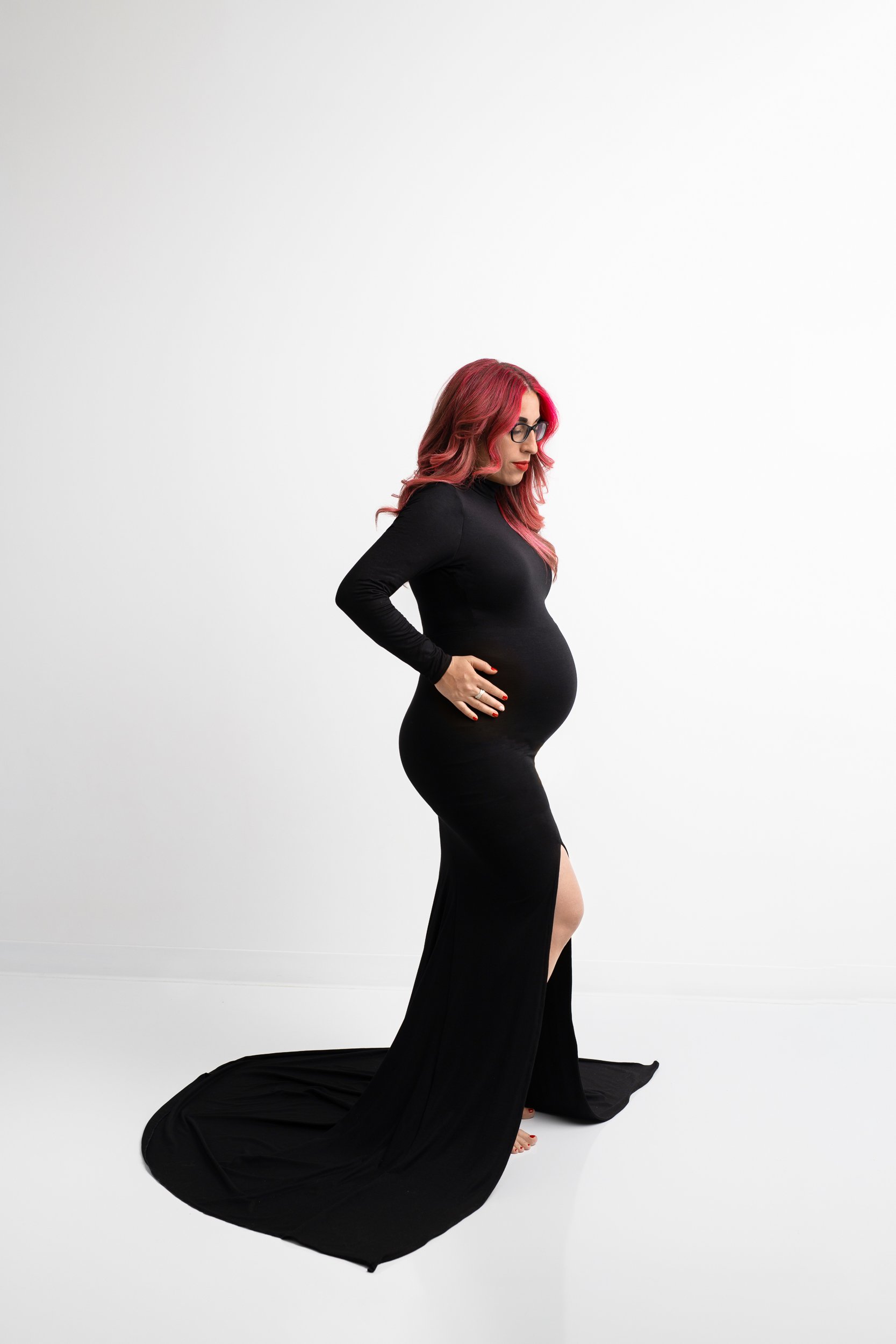  A woman with an elegant black gown and baby bump holds her stomach by Nicole Hawkins Photography. black fitted maternity pic gown #NicoleHawkinsPhotography #maternitysession #NJmaternityphotographer #NewJerseyphotographers #maternityphotos 