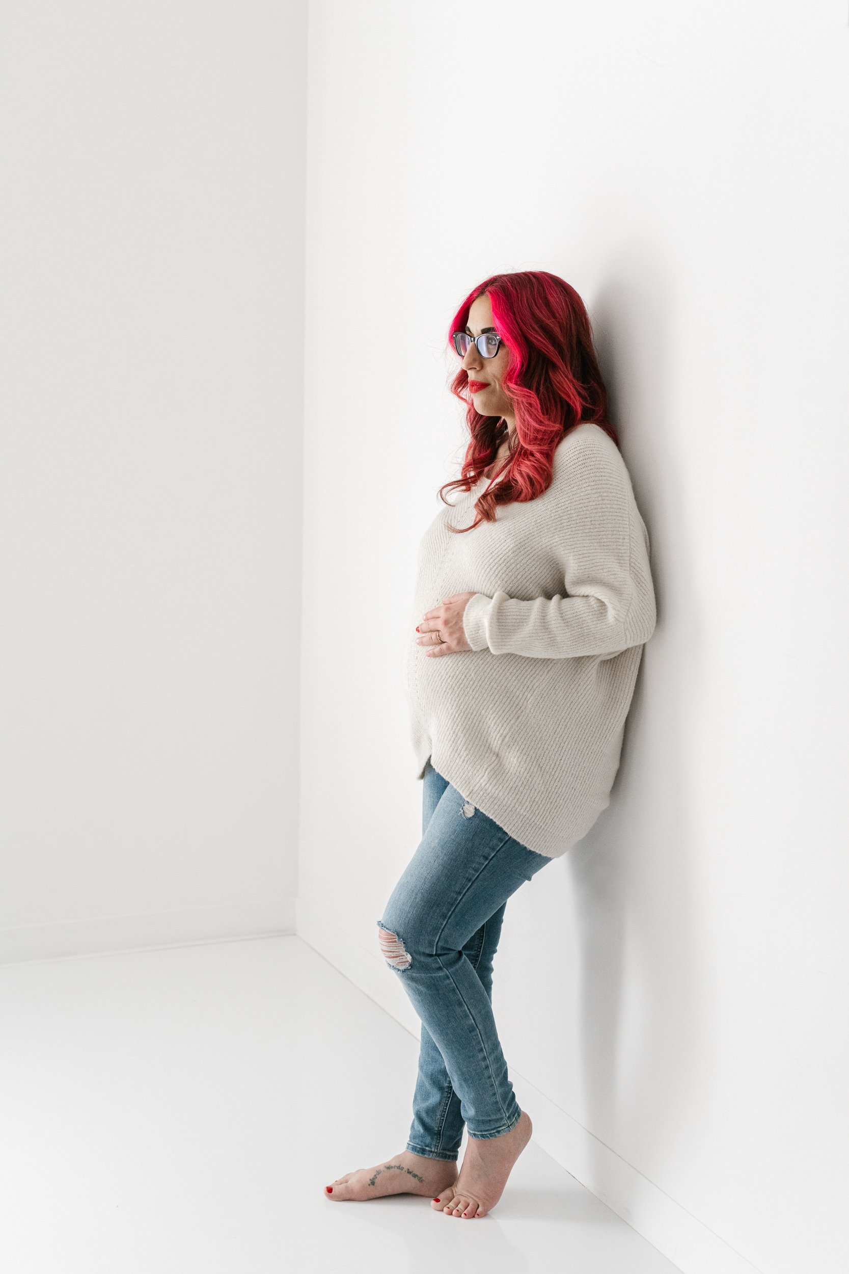  A pregnant woman wearing jeans and a sweater holds her belly by Nicole Hawkins Photography in NJ. maternity style maternity outfits NJ pics #NicoleHawkinsPhotography #maternitysession #NJmaternityphotographer #NewJerseyphotographers #maternityphotos