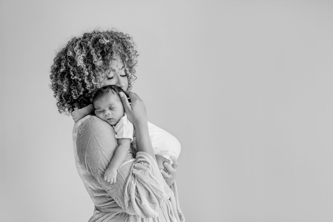  Mother with natural texture hair tenderly hugging newborn during photography session in Northern NJ.  