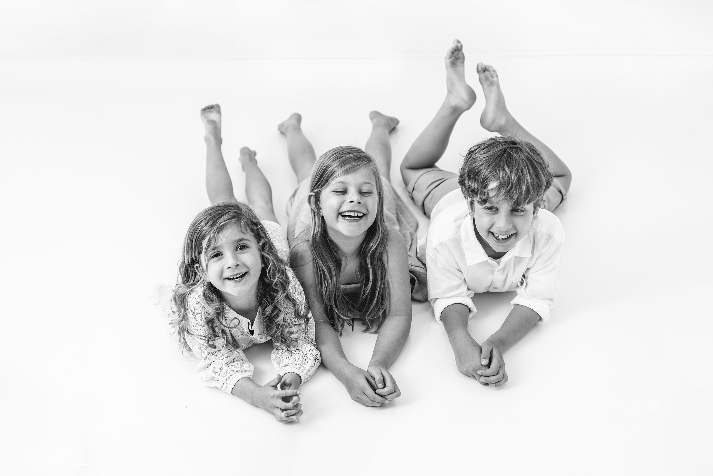  Three siblings on New Jersey photography studio floor naturally laughing. 