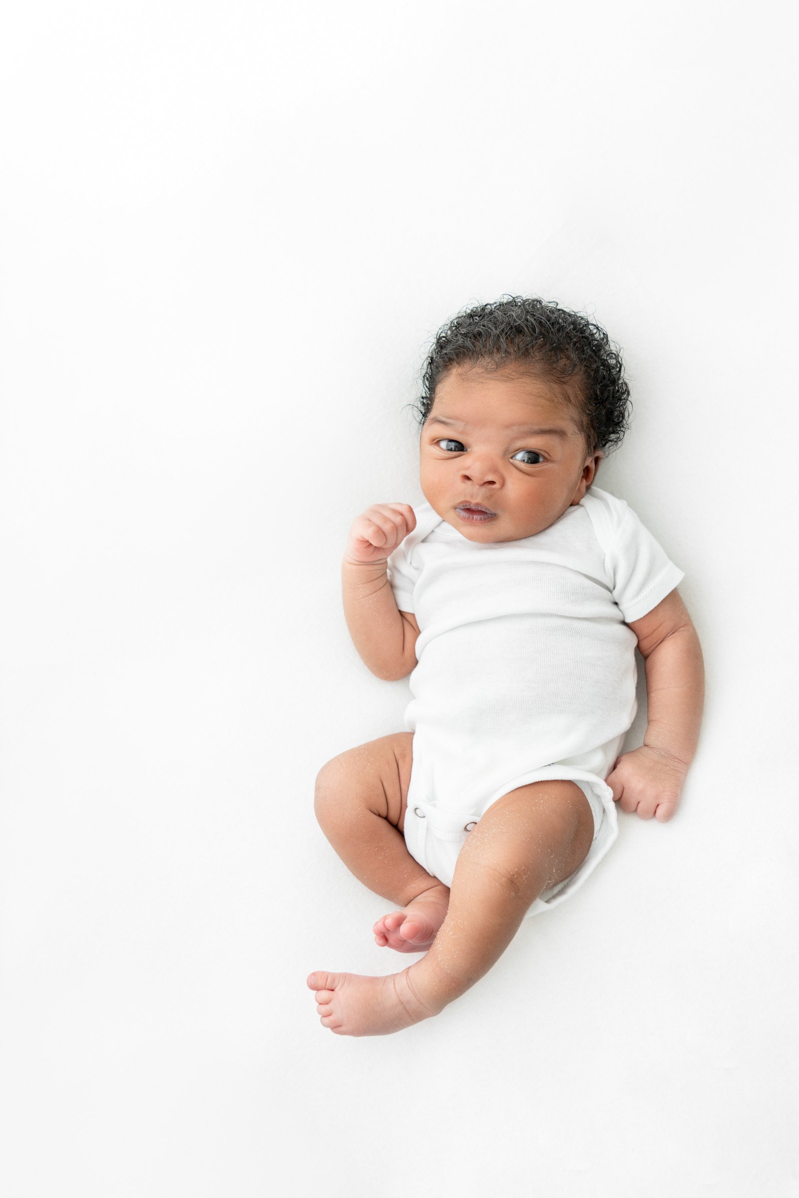  A little man in a white onesie during newborn studio session captured by professional photographer Nicole Hawkins Photography. NJ Photographer #nicolehawkinsphotography #NJbabyphotography #newbornportraits #NewJerseyStudioPhotography #newbornsession