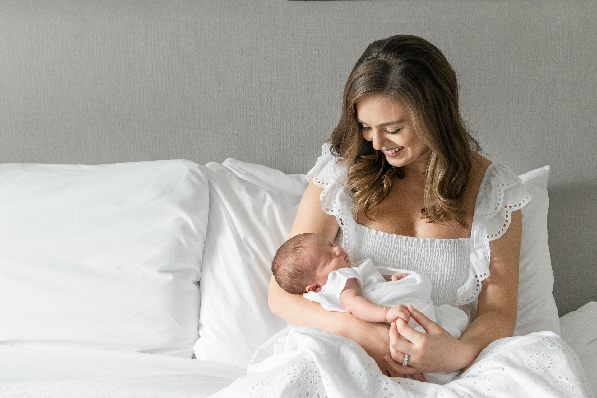  Nicole Hawkins Photography captures a mother sitting on her bed holding her newborn baby. New York City newborn photographer motherhood photo #nicolehawkinsphotography #NYCbabyphotography #newbornportraits #NewYorkStudioPhotography #newbornsession 