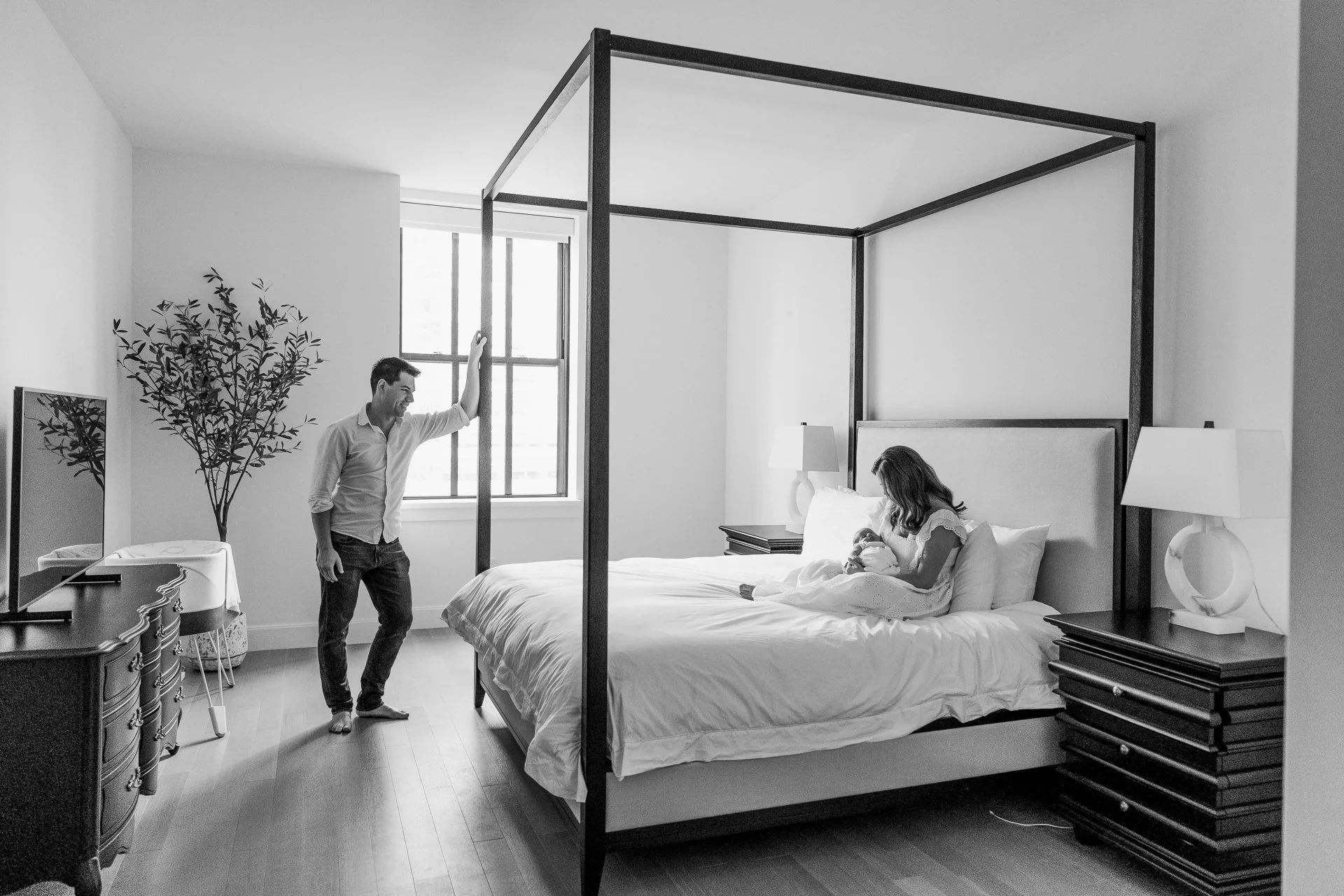  New York City newborn photographer Nicole Hawkins Photography captures a mother and father in a bedroom with their baby. Home newborn sessions #nicolehawkinsphotography #NYCbabyphotography #newbornportraits #NewYorkStudioPhotography #newbornsession 