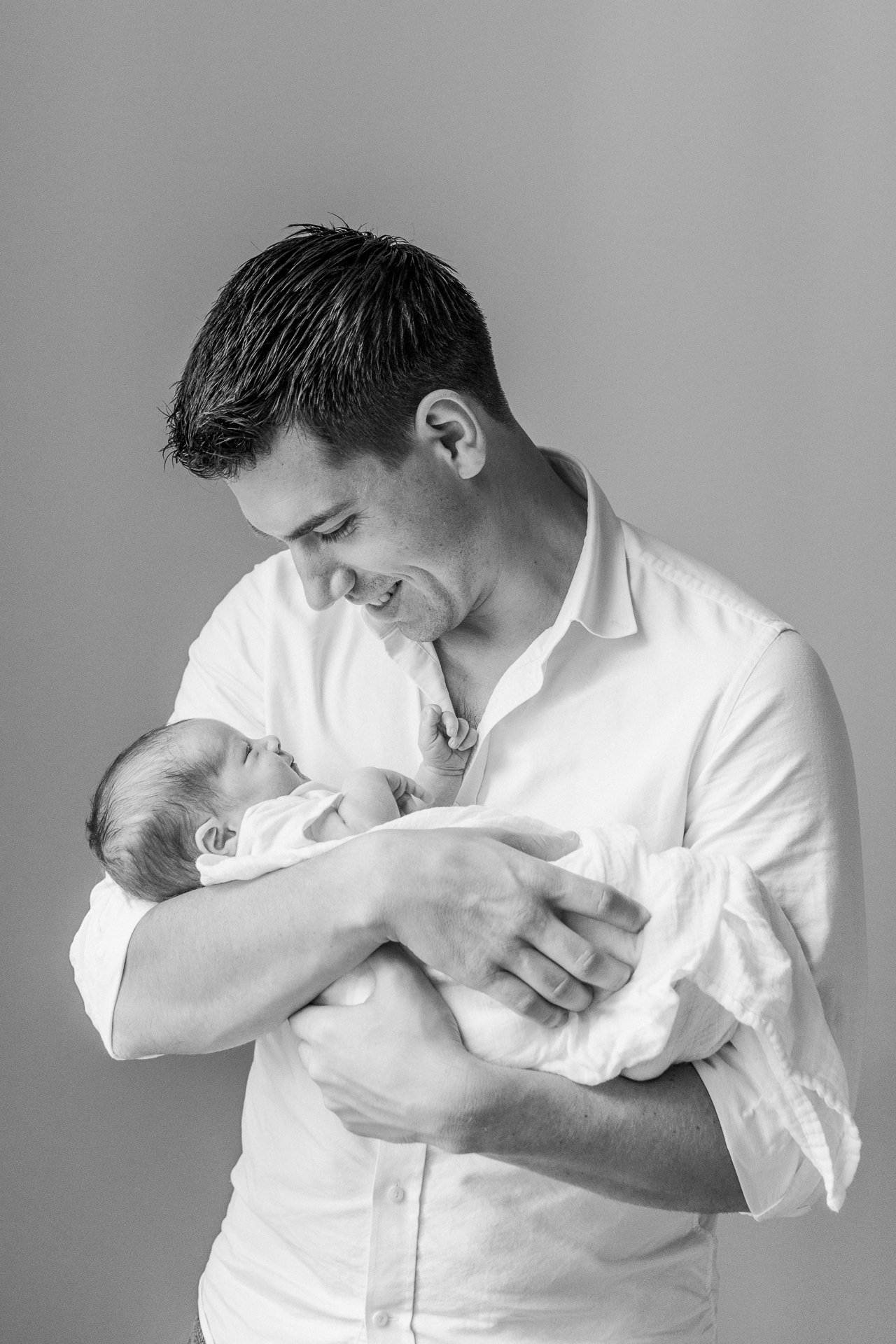  A father holds his swaddled baby boy smiling down at him by Nicole Hawkins Photography a newborn photographer. father with baby in-home portrait #nicolehawkinsphotography #NYCbabyphotography #newbornportrait #NewYorkStudioPhotography #newbornsession