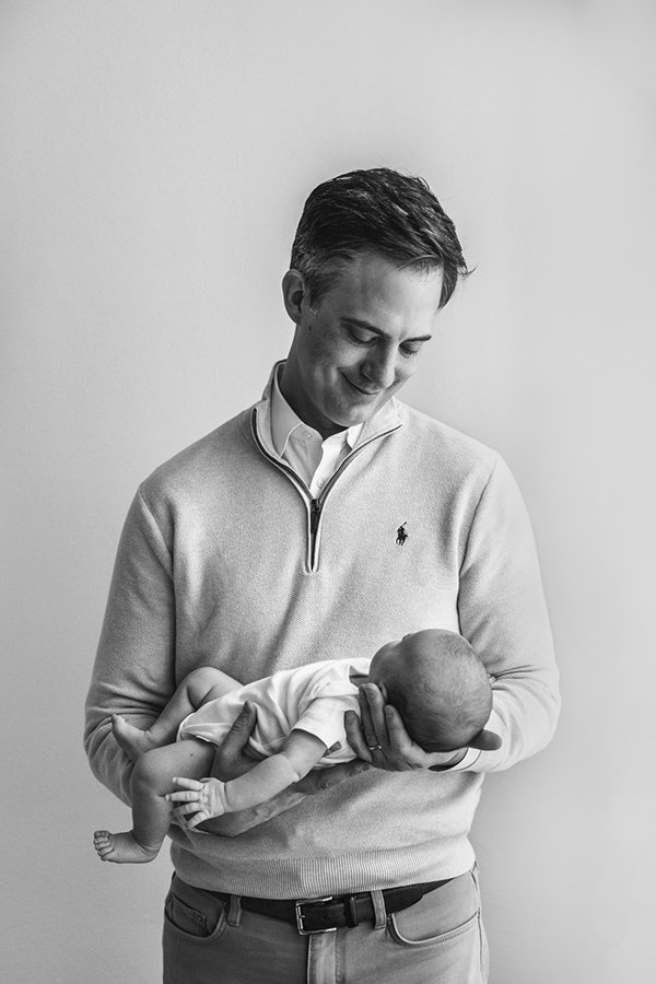 A father holds his newborn and smiles down at him by Nicole Hawkins Photography in New Jersey. father and newborn black and white #nicolehawkinsphotography #NJstudionewborns #newbornsession #studionewborns #NJnewbornphotographers #NJphotographers 
