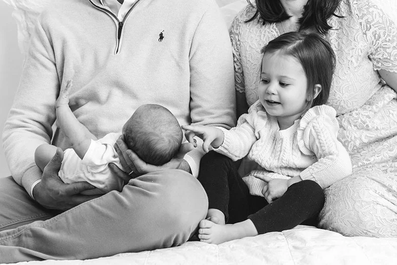  A black and white portrait of two young sisters sitting on their parent’s lap by Nicole Hawkins Photography. baby sister portrait #nicolehawkinsphotography #NJstudionewborns #newbornsession #studionewborns #NJnewbornphotographers #NJphotographers 