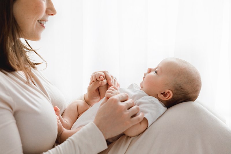  A mother holds a newborn on her knees and smiles by Nicole Hawkins Photography of New Jersey. mother and newborn baby on knees #nicolehawkinsphotography #NJstudionewborns #newbornsession #studionewborns #NJnewbornphotographers #NJphotographers 