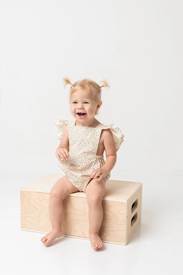  At a studio in New Jersey, Nicole Hawkins captures a little girl sitting on a box in a romper. floral rompers for toddlers #nicolehawkinsphotography #NJstudioportraits #babyportraits #babygirlportraits #NJbabyphotographers #NJphotographers 