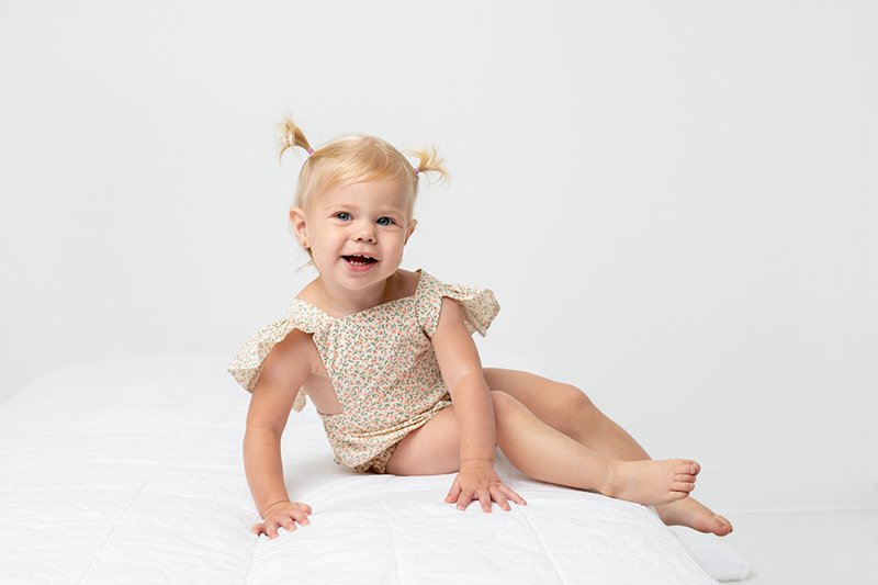  At a white wall studio, a baby girl is captured playing on a bed by Nicole Hawkins Photography. NJ baby photographers #nicolehawkinsphotography #NJstudioportraits #babyportraits #babygirlportraits #NJbabyphotographers #NJphotographers 