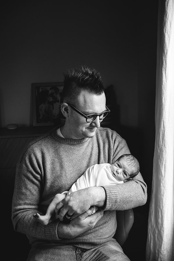  Nicole Hawkins Photography captures a black and white portrait of a father holding his new baby. portraits by the window father baby #nicolehawkinsphotography #NJfamilyphotographer #inhomenewbornsession #nicolehawkinsnewborns #NJnewbornphotography 