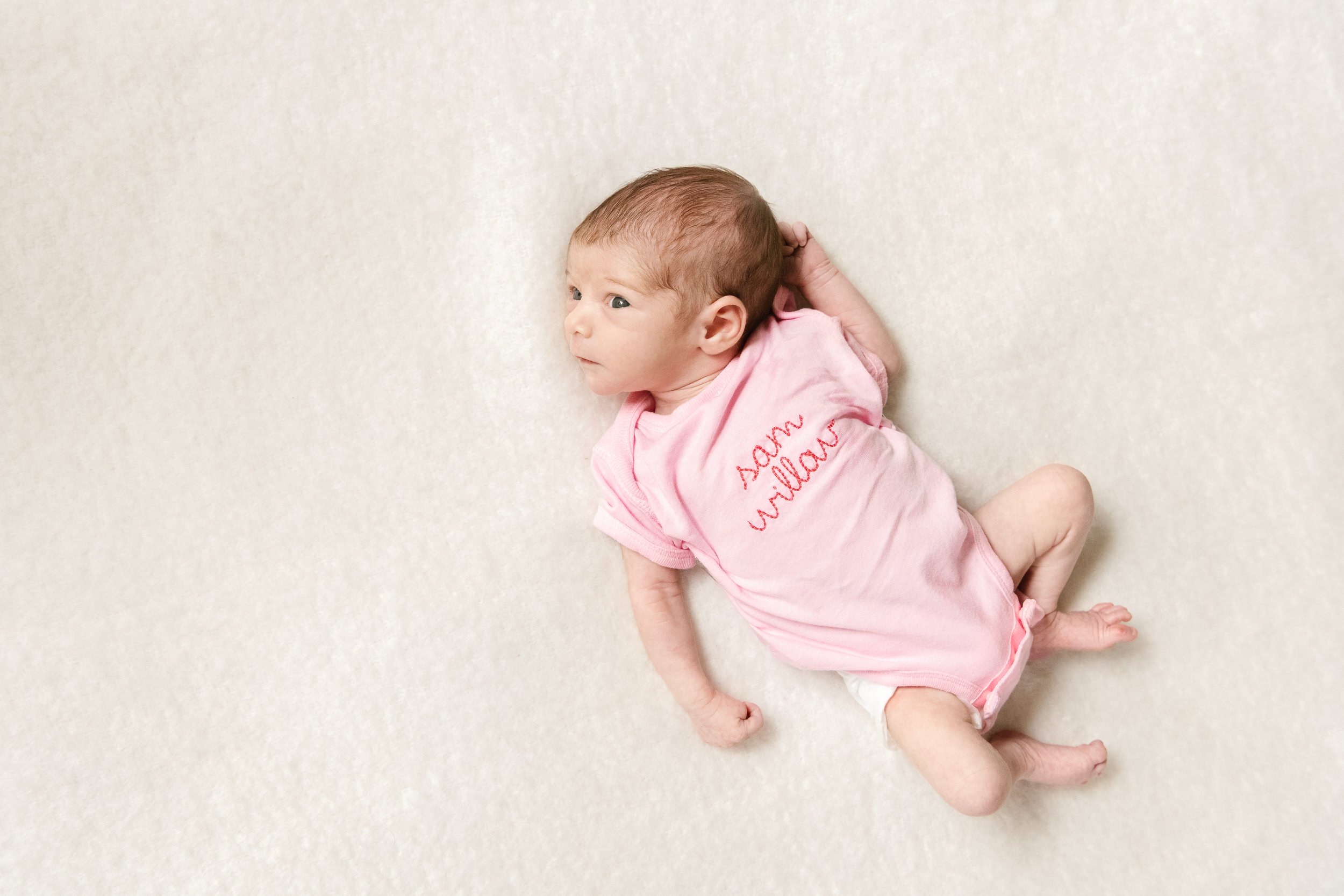  Baby girl in a pink onesie during an in-home newborn session with Nicole Hawkins Photography in Northern NJ. newborn baby portrait #nicolehawkinsphotography #NJfamilyphotographer #inhomenewbornsession #nicolehawkinsnewborns #NJnewbornphotography 
