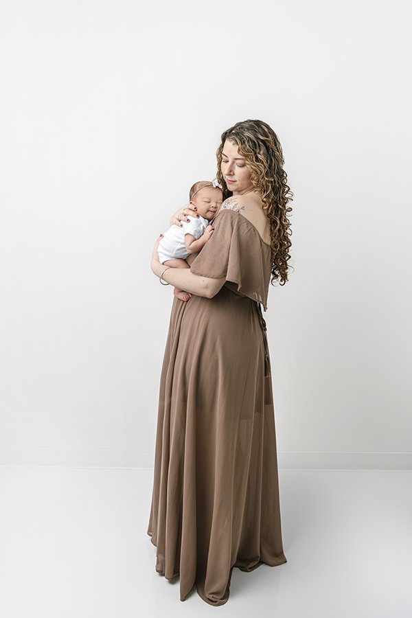  A mother in a brown dress holds her baby girl in a studio in NJ by Nicole Hawkins Photography. Maplewood NJ photography woman style ideas #NicoleHawkinsPhotography #studionewbornportraits #NJstudiophotographer #NJnewborns #NicoleHawkinsNewborns 