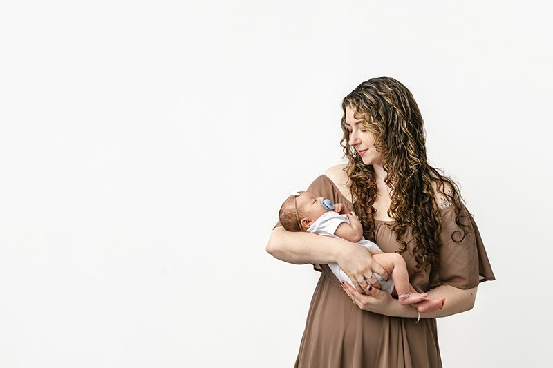  A mother with curly hair holds a brand new baby in a studio with Nicole Hawkins Photography in Maplewood, NJ. curly hair mother white studio #NicoleHawkinsPhotography #studionewbornportraits #NJstudiophotographer #NJnewborns #NicoleHawkinsNewborns 