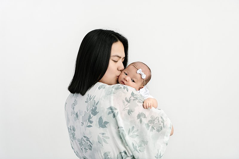  Asian mother kisses her baby girl in an all-white studio in NJ by Nicole Hawkins Photography. all-white studio family photoshoot #NicoleHawkinsPhotography #studionewbornportraits #NJstudiophotographer #NJnewborns #NicoleHawkinsNewborns 