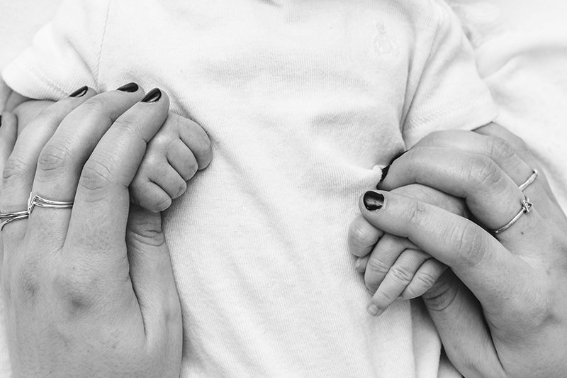  A black and white portrait of a mother holding her baby girl's hands by Nicole Hawkins Photography. the baby hand being held by a mother and baby #NicoleHawkinsPhotography #studionewbornportraits #NJstudiophotographer #NJnewborns #NicoleHawkinsNewbo
