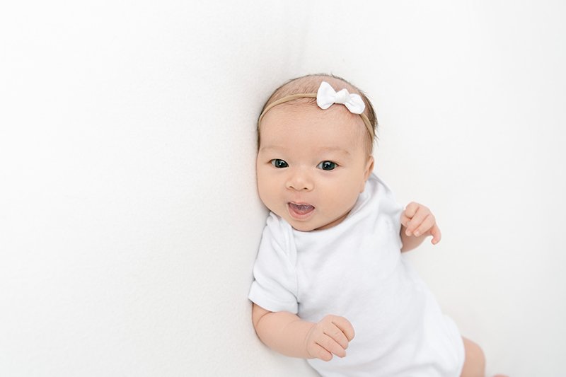  In Maplewood, New Jersey at a studio Nicole Hawkins Photography captures a baby girl smiling in her white onesie. white onesie smiling baby #NicoleHawkinsPhotography #studionewbornportraits #NJstudiophotographer #NJnewborns #NicoleHawkinsNewborns 