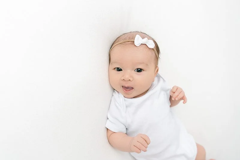 In Maplewood, New Jersey at a studio Nicole Hawkins Photography captures a baby girl smiling in her white onesie. white onesie smiling baby #NicoleHawkinsPhotography #studionewbornportraits #NJstudiophotographer #NJnewborns #NicoleHawkinsNewborns 