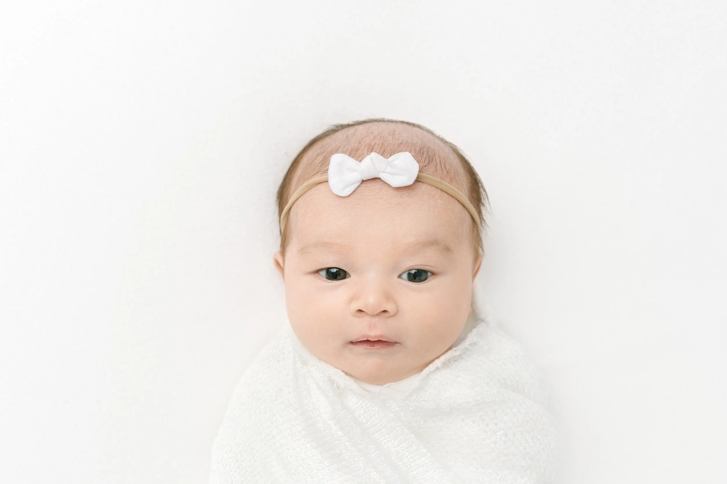  Baby girl with eyes wide open wearing a white bow captured by NJ newborn photographer Nicole Hawkins Photography. baby with eyes open white bow #NicoleHawkinsPhotography #studionewbornportraits #NJstudiophotographer #NJnewborns #NicoleHawkinsNewborn