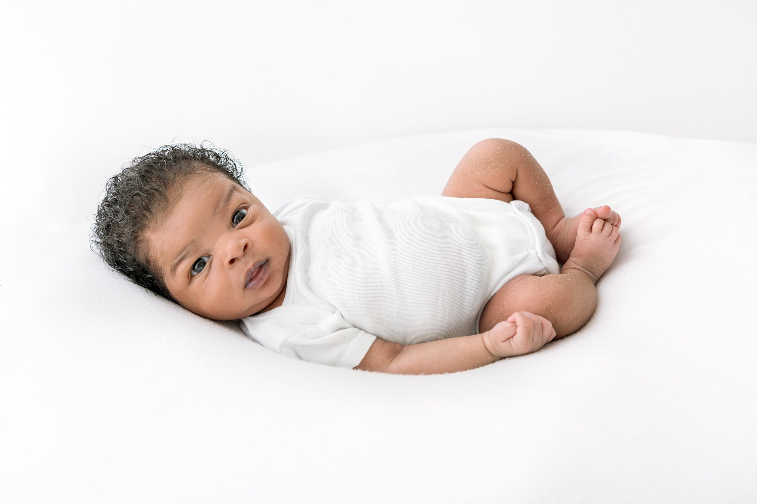  Awake baby in white onesie in New Jersey newborn photography studio. 
