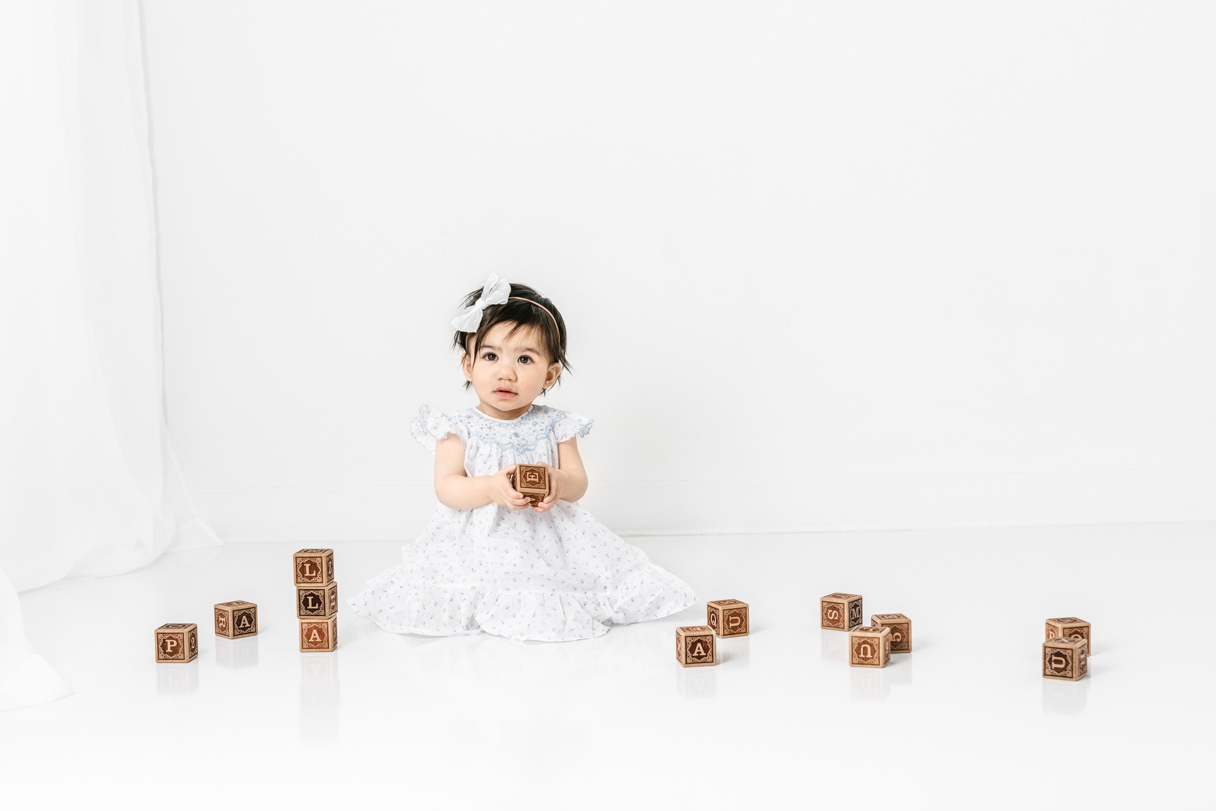  Little girl playing with wooden blocks in a white studio in New Jersey by Nicole Hawkins Photography. baby with blocks white studio #nicolehawkinsphotography #nicolehawkinsbirthday #nicolehawkinsportraits #NJstudiophotography #1stbirthday 