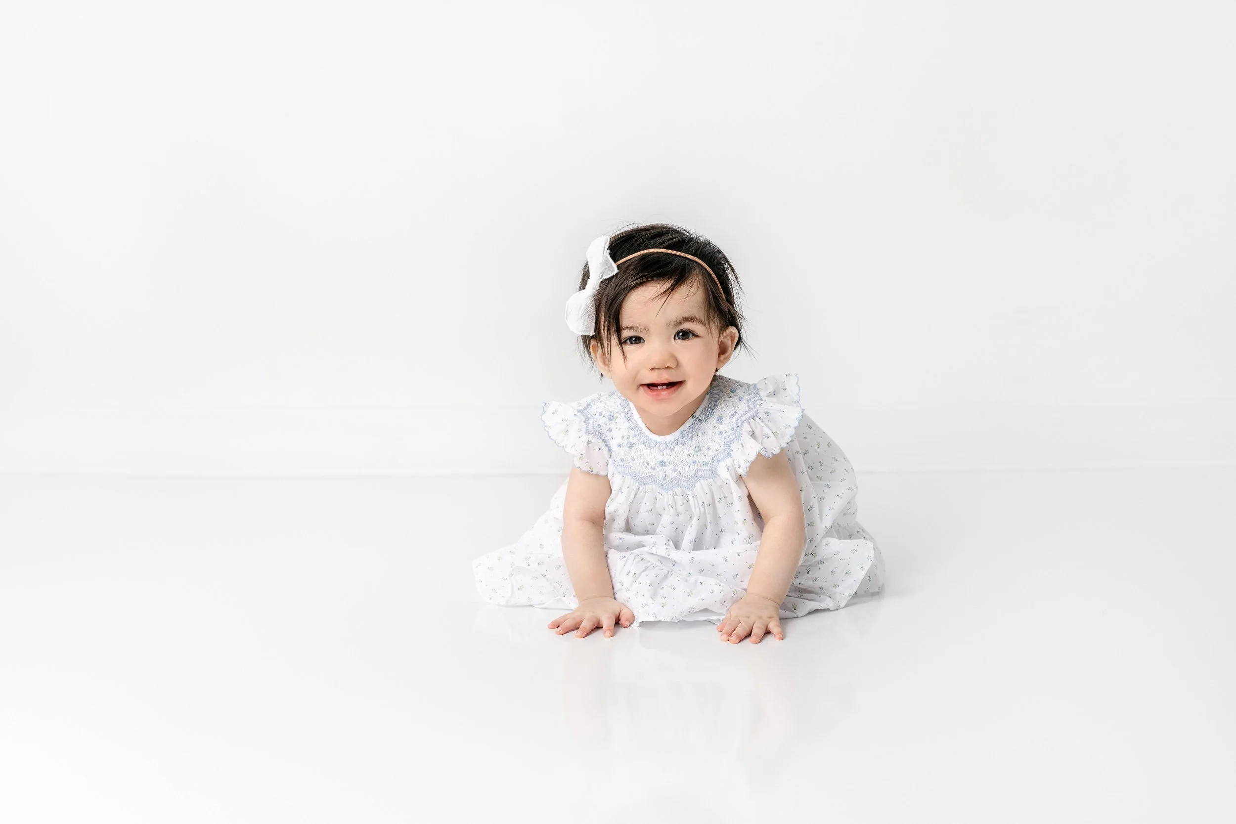 A dark-haired little girl in a blue floral outfit by Nicole Hawkins Photography in New Jersey. crawling baby milestone portraits girl #nicolehawkinsphotography #nicolehawkinsbirthday #nicolehawkinsportraits #NJstudiophotography #1stbirthday 