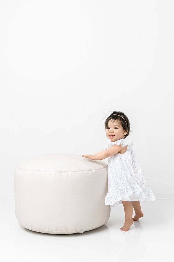  In a bright white New Jersey studio, a little girl stands by a cushion by Nicole Hawkins Photography. bright studio NJ portrait photographer #nicolehawkinsphotography #nicolehawkinsbirthday #nicolehawkinsportraits #NJstudiophotography #1stbirthday 