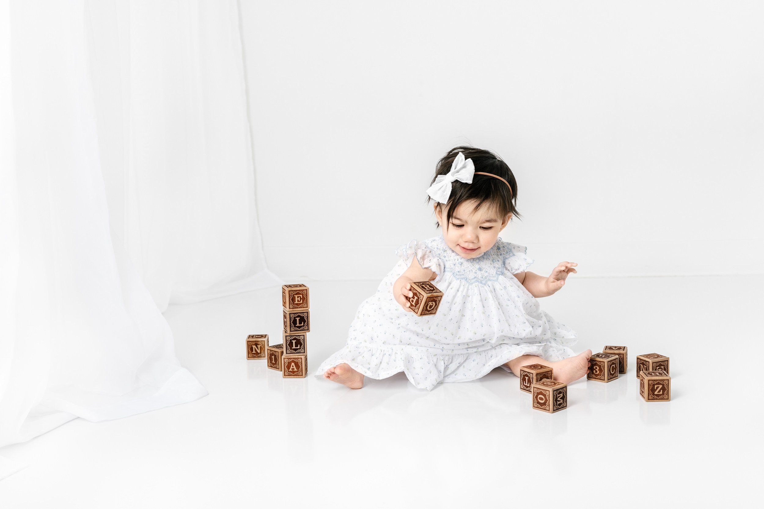  Baby girl with wooden letter blocks playing on the floor captured by Nicole Hawkins Photography in NJ. wooden block baby portraits #nicolehawkinsphotography #nicolehawkinsbirthday #nicolehawkinsportraits #NJstudiophotography #1stbirthday 