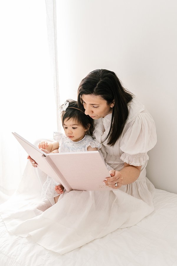  A mother reads to her baby girl in a New Jersey Studio by Nicole Hawkins Photography. mother and baby reading book together with baby girl #nicolehawkinsphotography #nicolehawkinsbirthday #nicolehawkinsportraits #NJstudiophotography #1stbirthday 