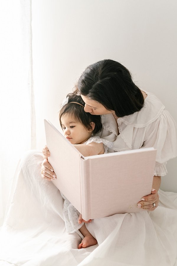  The little girl looks at a book with her mother captured by New Jersey family photographer Nicole Hawkins Photography. motherhood portrait #nicolehawkinsphotography #nicolehawkinsbirthday #nicolehawkinsportraits #NJstudiophotography #1stbirthday 