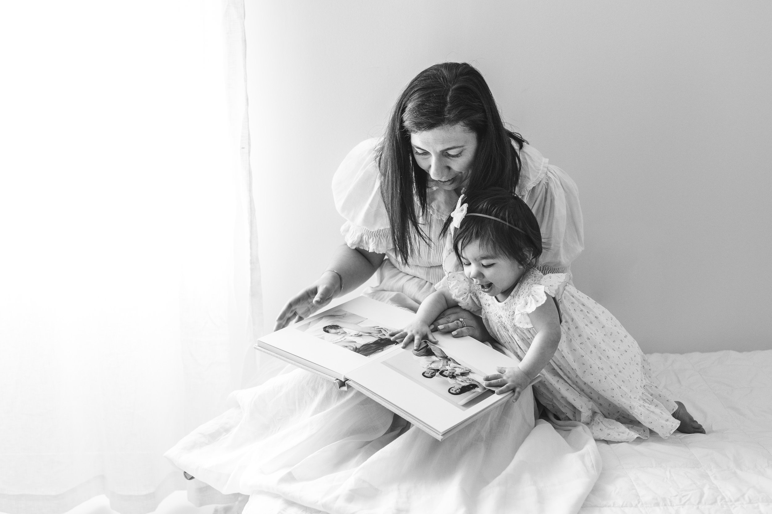  Black and white portrait of a mother and child looking at baby pictures by Nicole Hawkins Photography. mother and baby girl NJ photographers #nicolehawkinsphotography #nicolehawkinsbirthday #nicolehawkinsportraits #NJstudiophotography #1stbirthday 