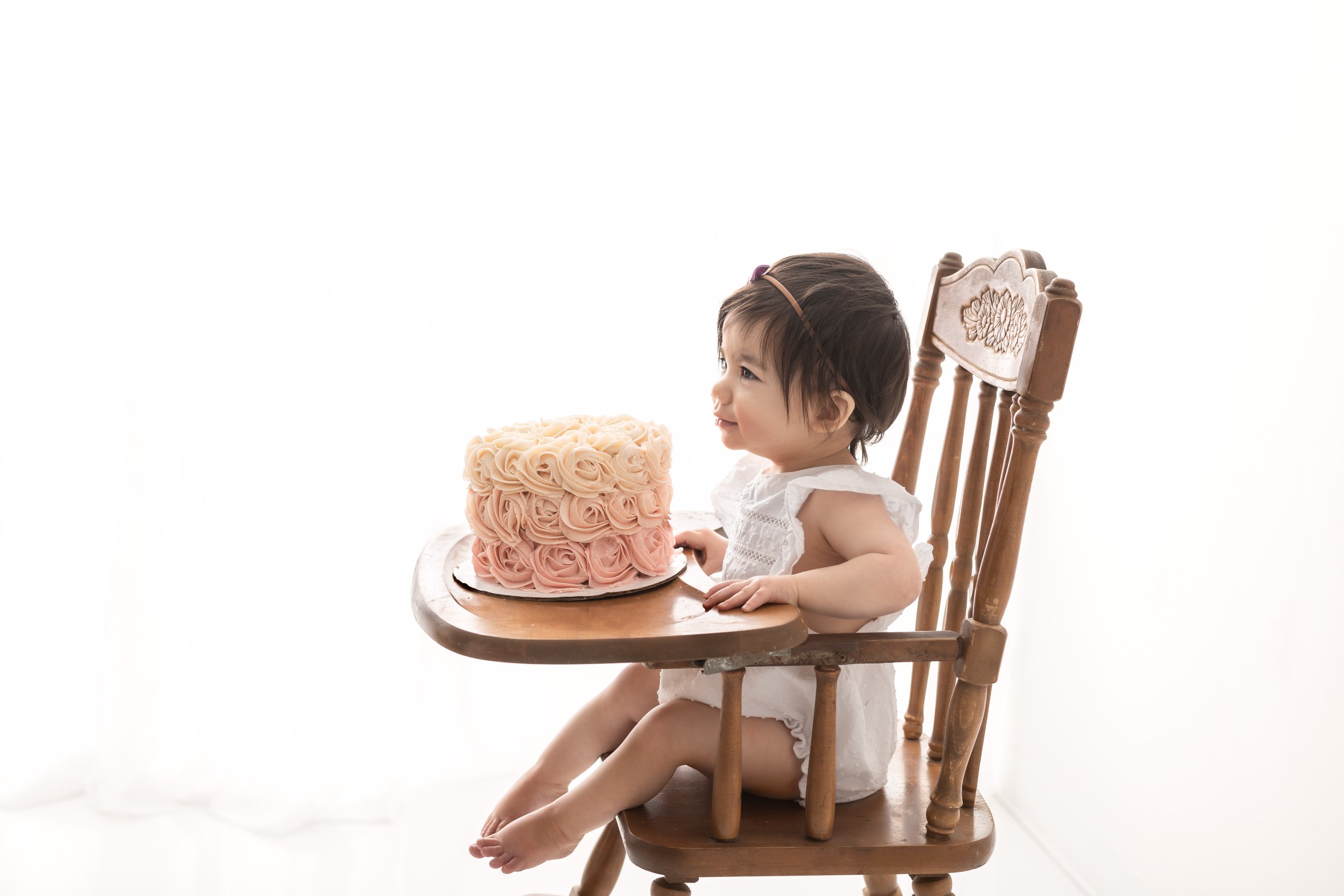  Sitting in an antique high chair a babysits with her smash cake in a New Jersey studio by Nicole Hawkins Photography. antique high chair smash #nicolehawkinsphotography #nicolehawkinsbirthday #nicolehawkinsportraits #NJstudiophotography #1stbirthday