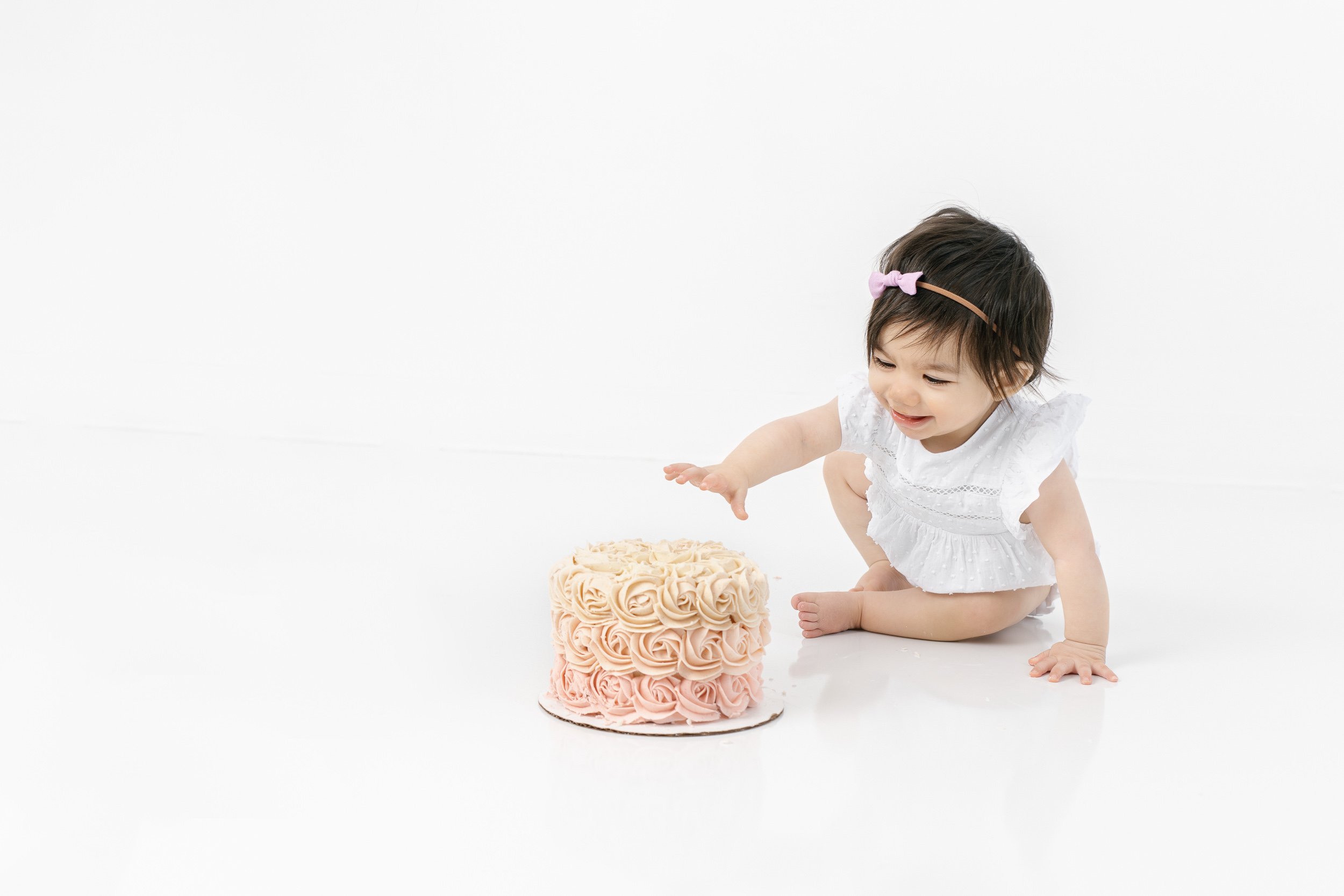  A little girl reaches for her pink ombre smash cake during a studio session with Nicole Hawkins Photography. pink ombre smash cake portraits #nicolehawkinsphotography #nicolehawkinsbirthday #nicolehawkinsportraits #NJstudiophotography #1stbirthday 