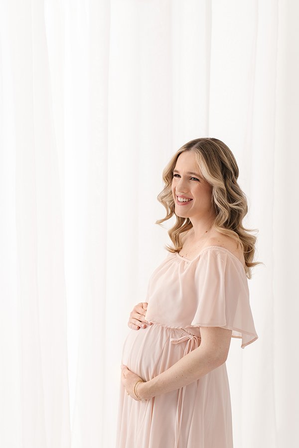  A mother-to-be holds her baby bump in front of a bright light window in New Jersey by Nicole Hawkins Photography. a mother holds her bump #nicolehawkinsphotography #nicolehawkinsmaternity #maternityportraits #NJstudiophotography #mommatobe 