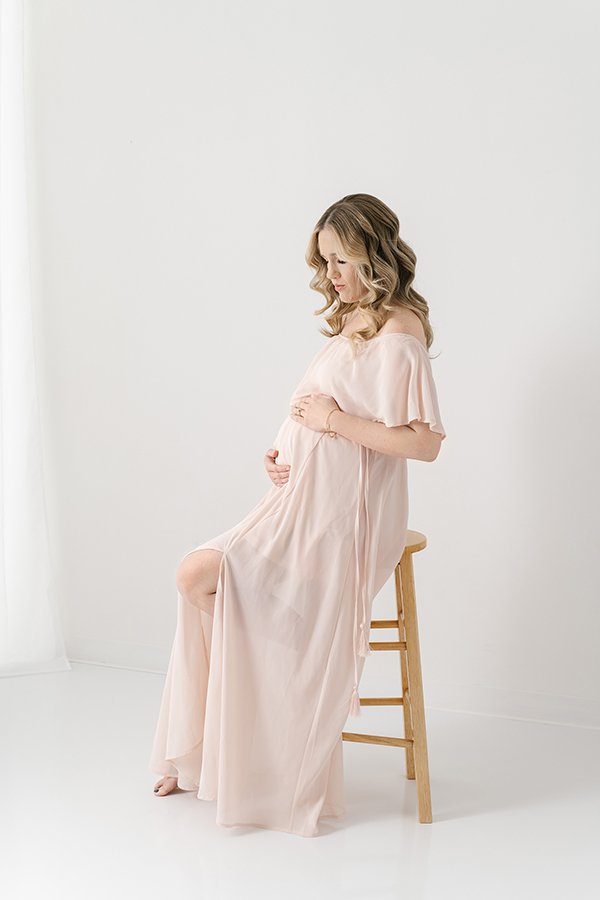  A pregnant woman in a pink flowy gown holding her bump was captured by Nicole Hawkins Photography. New Jersey maternity photographer bump pic #nicolehawkinsphotography #nicolehawkinsmaternity #maternityportraits #NJstudiophotography #mommatobe 