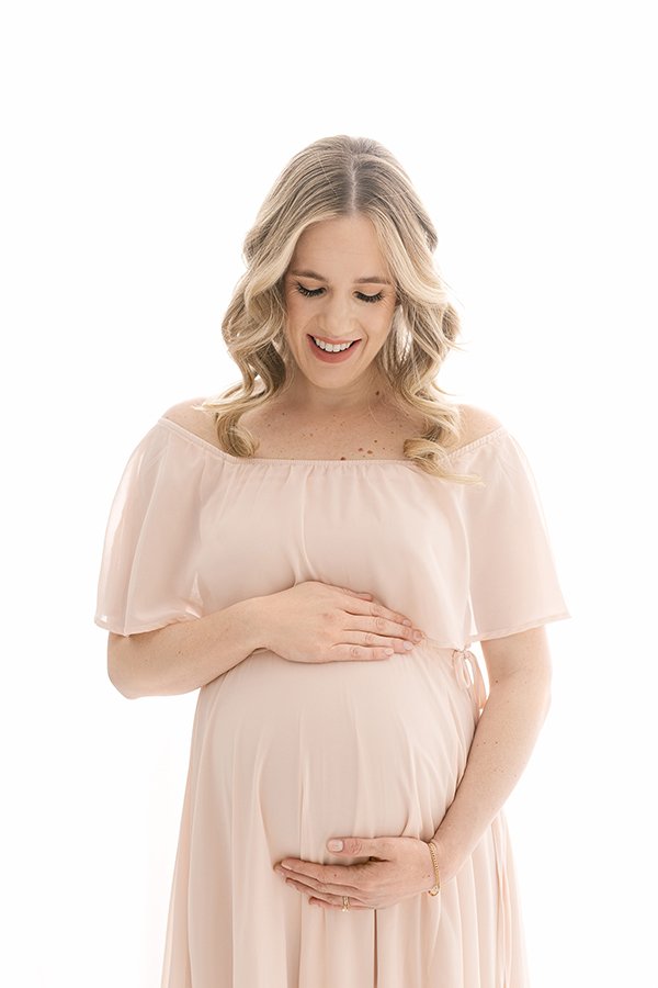  A woman in a New Jersey studio wearing a flowy gown holds her pregnant belly by Nicole Hawkins Photography. studio maternity New Jersey photog #nicolehawkinsphotography #nicolehawkinsmaternity #maternityportraits #NJstudiophotography #mommatobe 