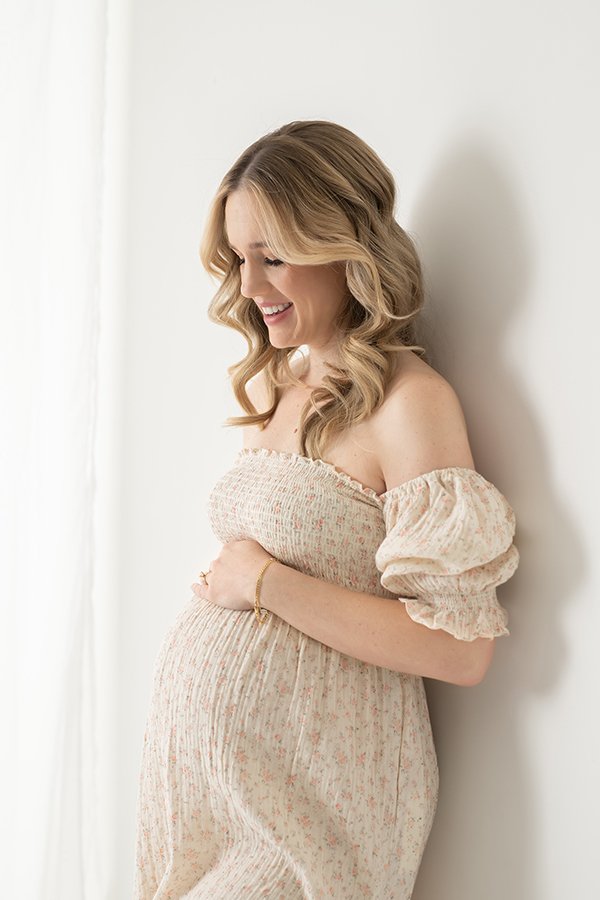  In a spring maternity gown, a mother looks lovingly at her baby bump by Nicole Hawkins Photography. baby on the way mother loving look momma to be #nicolehawkinsphotography #nicolehawkinsmaternity #maternityportraits #NJstudiophotography #mommatobe 