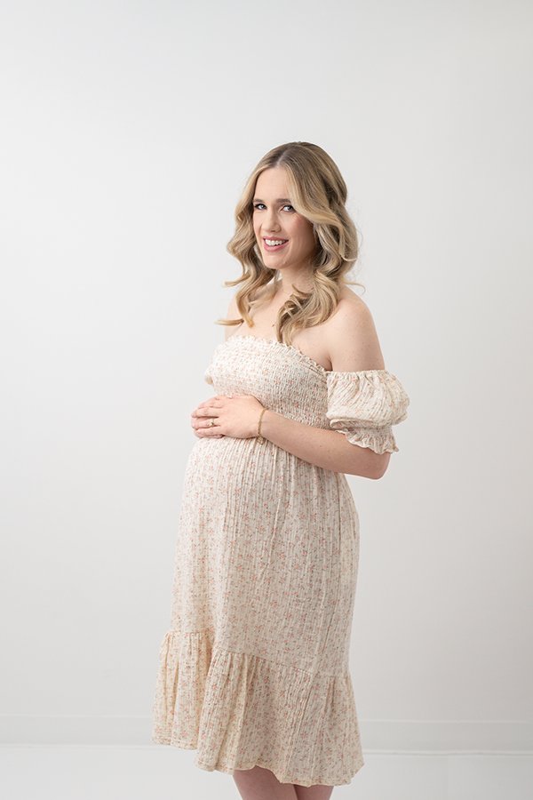  A beautiful pregnant woman in an ivory floral dress holds her bump by Nicole Hawkins Photography. ivory maternity gown New Jersey portraits #nicolehawkinsphotography #nicolehawkinsmaternity #maternityportraits #NJstudiophotography #mommatobe 