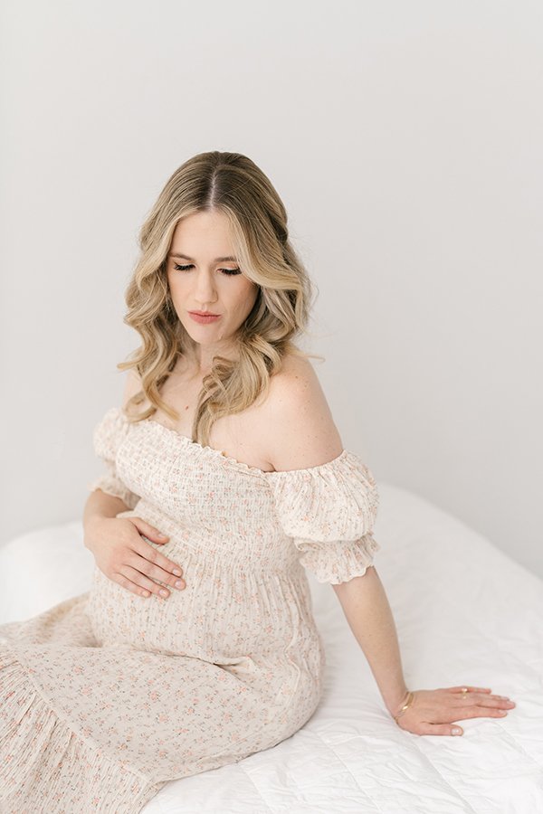 A mother sitting on a bed holds her belly in New Jersey by Professional Nicole Hawkins Photography. Professional New Jersey Photographer belly bump #nicolehawkinsphotography #nicolehawkinsmaternity #maternityportraits #NJstudiophotography #mommatobe