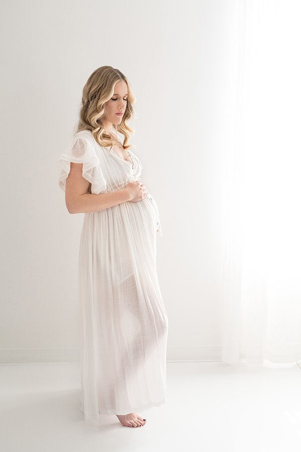  A pregnant woman wearing a sheer white dress for a maternity session with Nicole Hawkins Photography. sheer maternity outfit studio NJ maternity #nicolehawkinsphotography #nicolehawkinsmaternity #maternityportraits #NJstudiophotography #mommatobe 