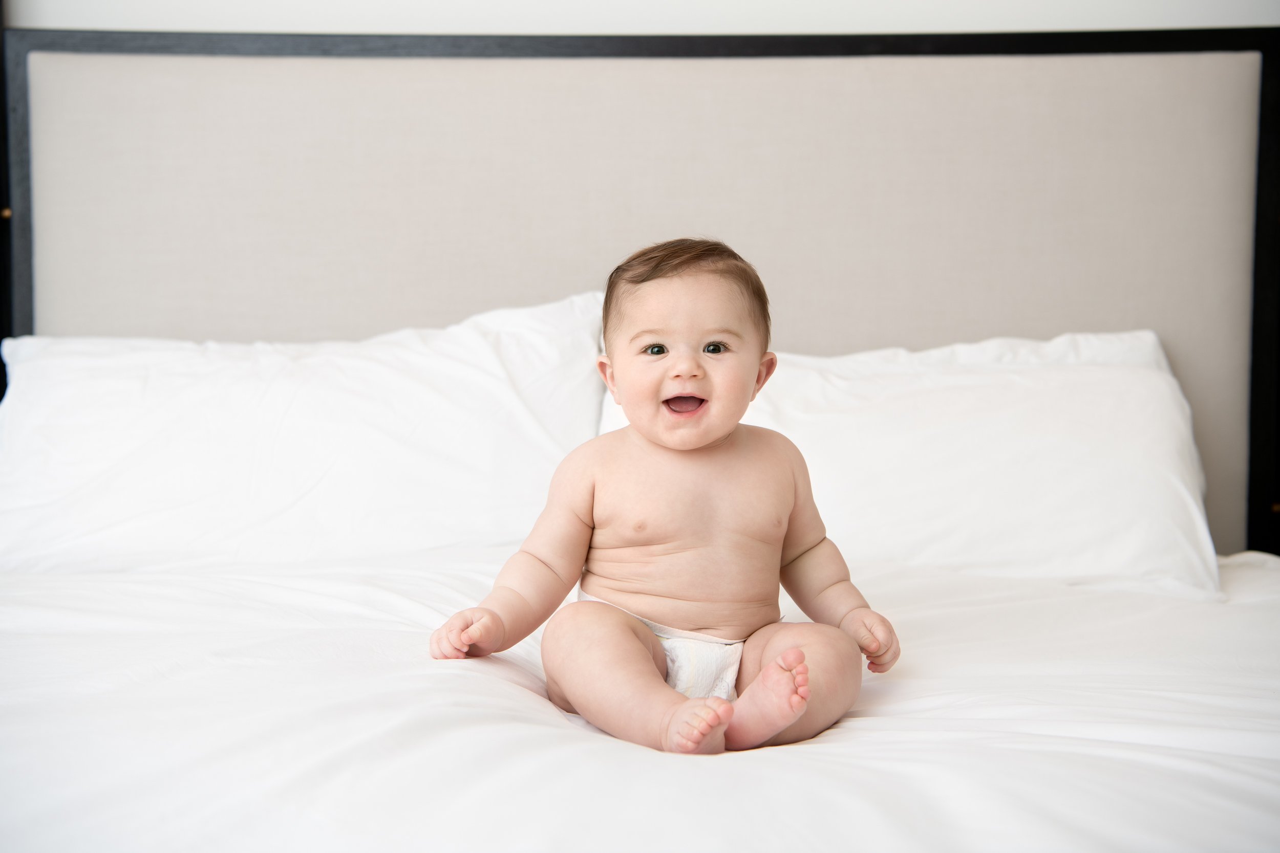  Sixth-month-old baby sitting on the bed in a diaper during a milestone session with Nicole Hawkins Photography. baby on the bed #NicoleHawkinsPhotography #NicoleHawkinsMilestones #BabyMilestoneSession #NJfamilyphotographer #Inhome #babyportraits 