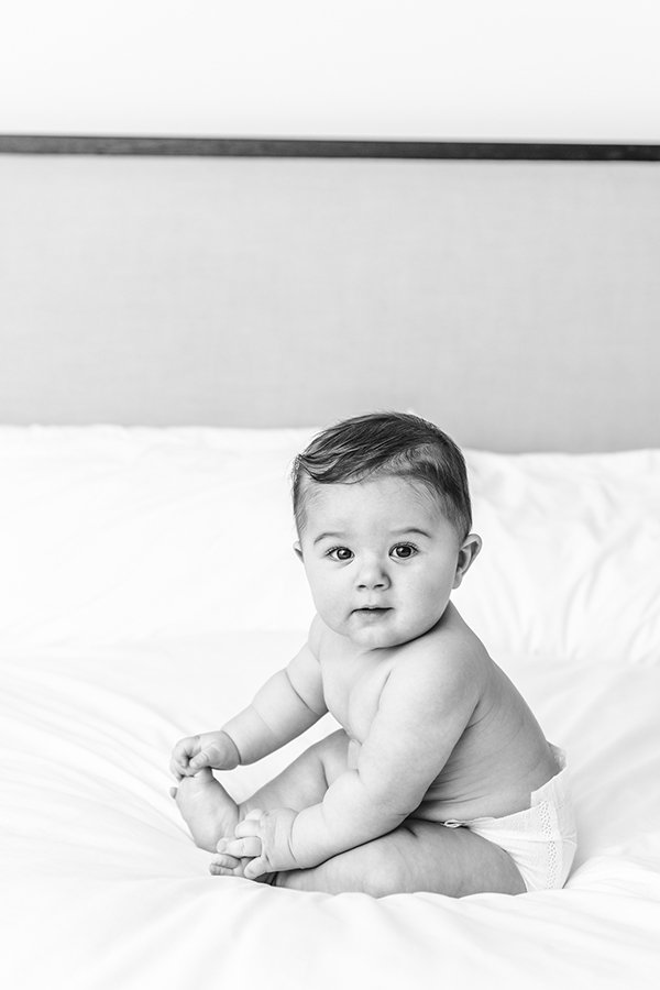  A Black and white portrait of a baby sitting on a bed was captured by Nicole Hawkins Photography. baby milestones NJ #NicoleHawkinsPhotography #NicoleHawkinsMilestones #BabyMilestoneSession #NJfamilyphotographer #Inhomephotography #babyportraits 