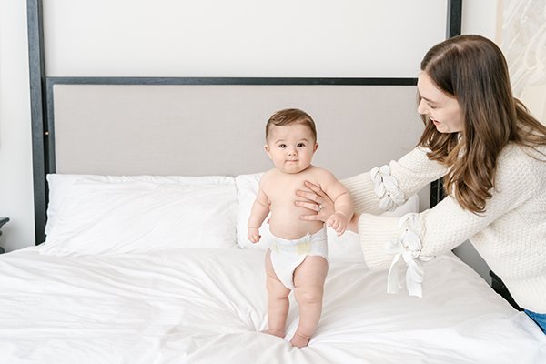  A mother holds her baby boy on a white bed during an in-home session in NJ, with Nicole Hawkins Photography. in-home #NicoleHawkinsPhotography #NicoleHawkinsMilestones #BabyMilestoneSession #NJfamilyphotographer #Inhomephotography #babyportraits 