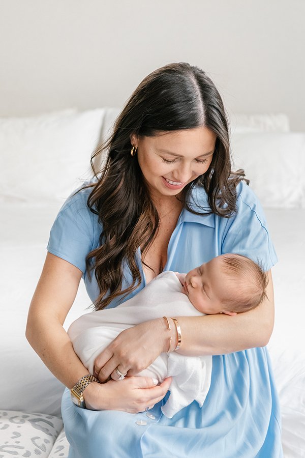  A mother in a blue dress holds her sleeping baby captured by New Jersey photographer Nicole Hawkins Photography. blue mothers dress #NewbornSession #NJfamilyphotographer #Inhomebabyphotography #newborn #NicoleHawkinsPhotography #NicoleHawkinsNewborn